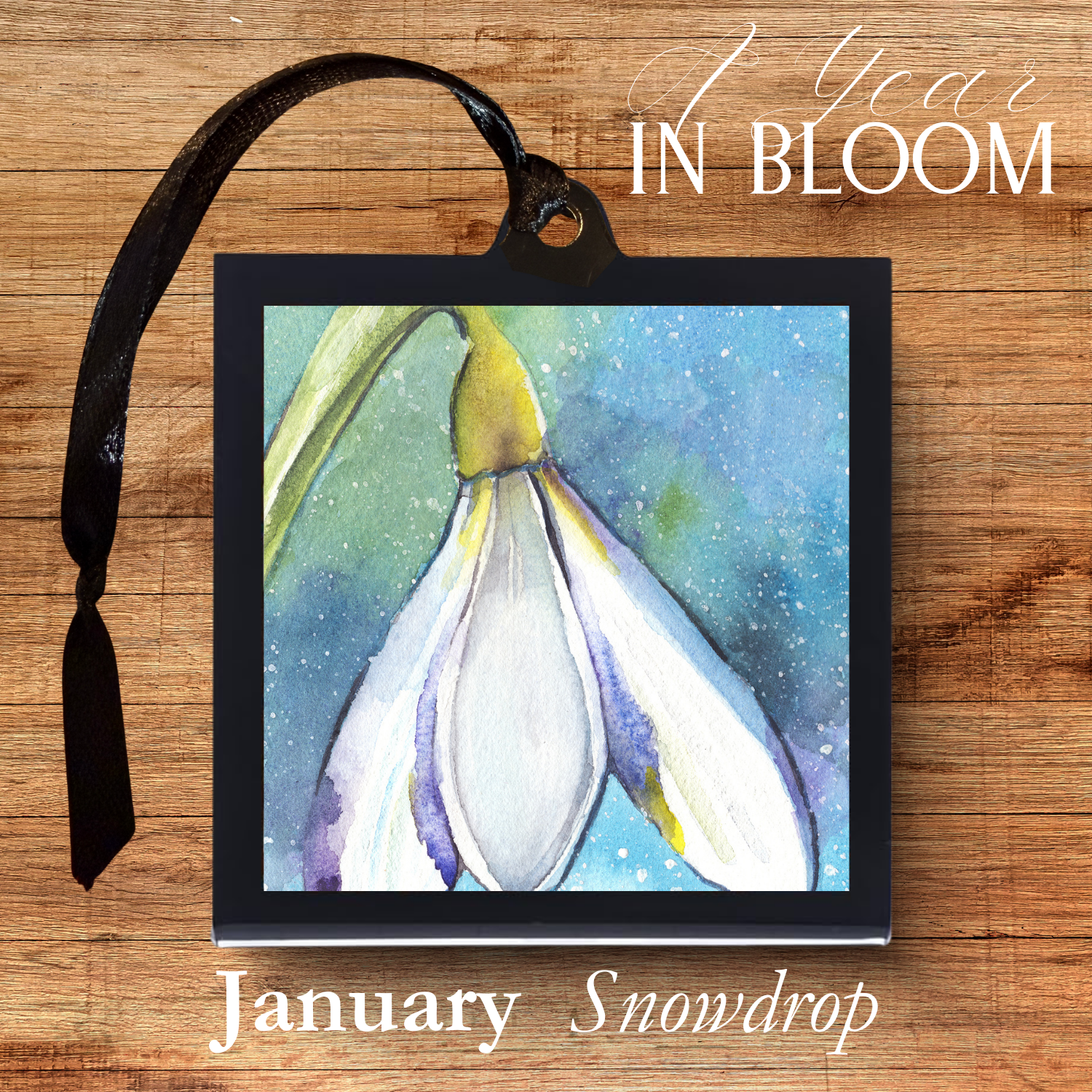 Framed artwork of a snowdrop with '1 Year in Bloom' text on a wooden background