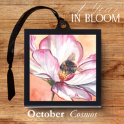 Framed artwork of a pink flower with a bee on a wooden surface, labeled 'October Cosmos'.