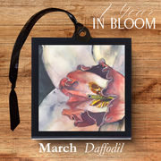 Framed artwork of a daffodil with '1 Year in Bloom' text on a wooden surface