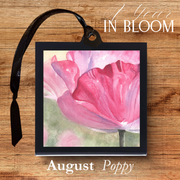 Framed artwork of a pink flower with 'August Poppy' text on a wooden background
