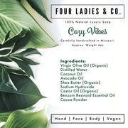 Product label for 'Cozy Vibes' soap from Four Ladies & Co. with green leaves in the background.