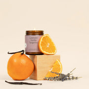 Candle labeled 'Lavender Vanilla Tangerine' with oranges and lavender on a beige background