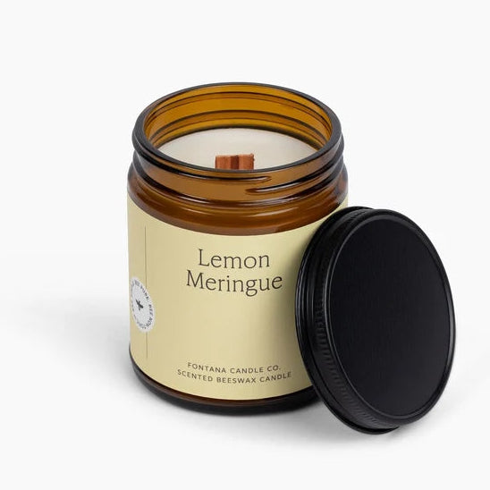 An amber glass jar candle with a cream label reading 'Lemon Meringue' and a black lid leaning against it, photographed on a clean white background. The label also shows the brand name Fontana Candle Co.