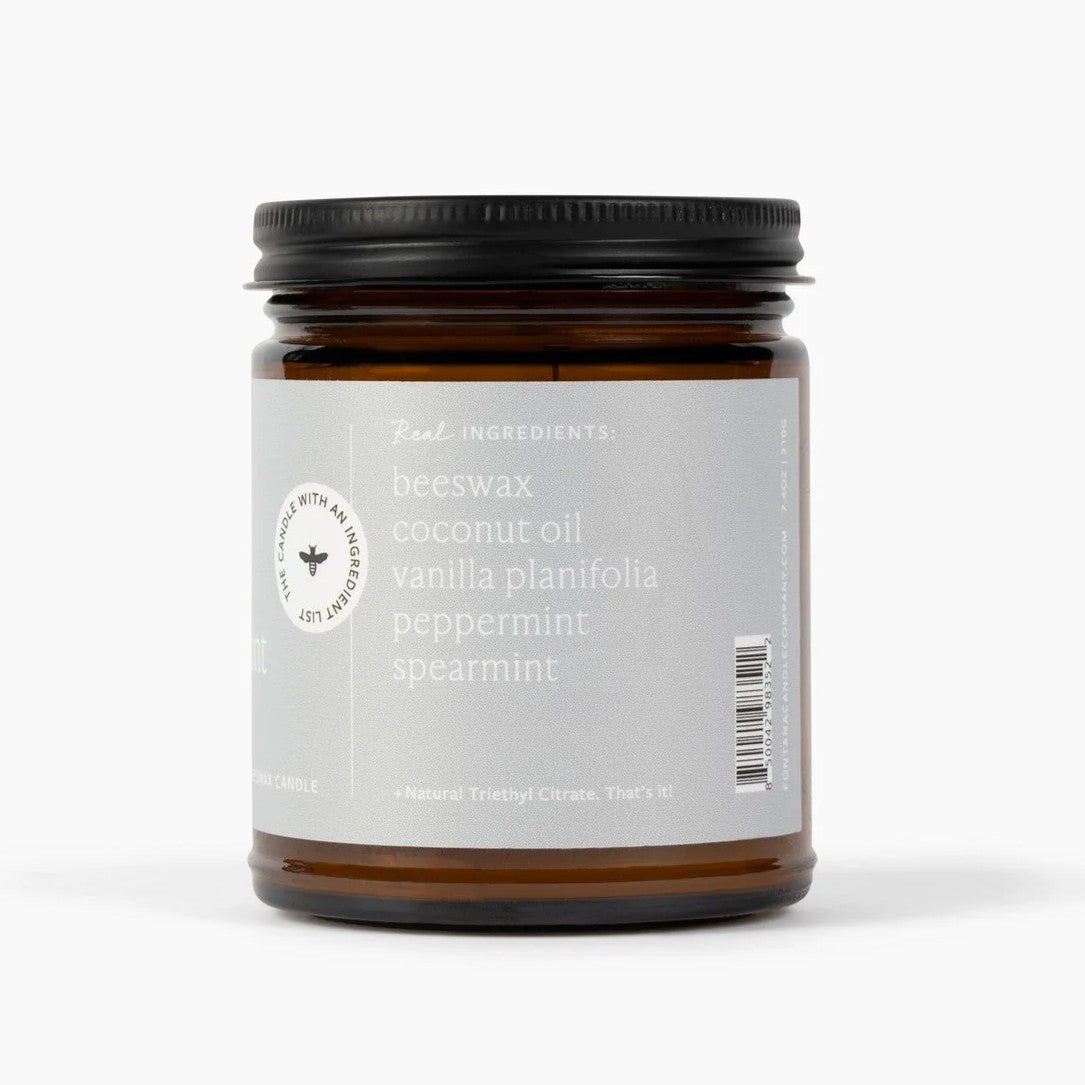 An amber glass jar candle with a black metal lid and a light gray label, photographed on a clean white background. The label reads 'Real Ingredients: beeswax coconut oil vanilla planifolia peppermint spearmint'.