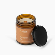 An open amber glass candle jar labeled Fontana Candle Co. Pumpkin Pie, with a black lid leaning against it on a clean white background.