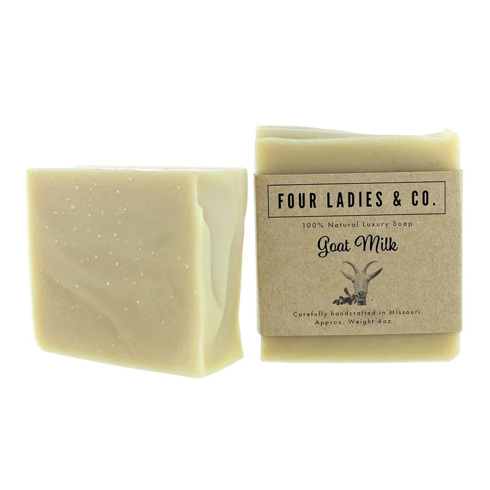 A bar of goat milk soap next to its kraft paper packaging label, both from Four Ladies & Co., on a solid white background.