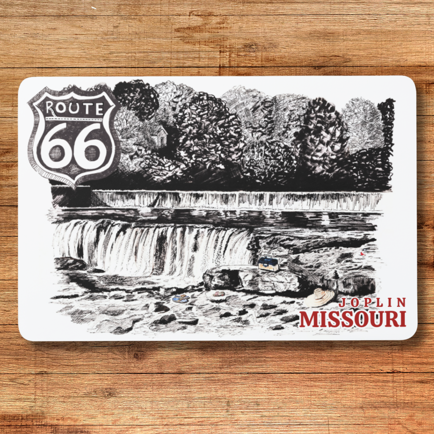 Placemat with Route 66 design featuring a waterfall and Joplin, Missouri text on a wooden surface.