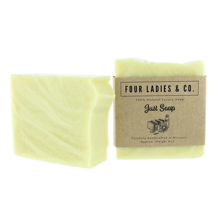 A pale yellow bar of soap shown next to its kraft paper packaging label, which reads 'FOUR LADIES & CO. Just Soap'.