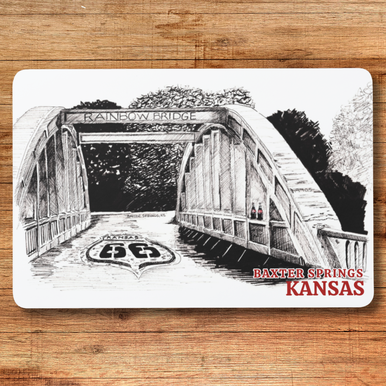 Illustration of a bridge with 'Rainbow Bridge' and 'Baxter Springs, Kansas' text on a wooden surface.