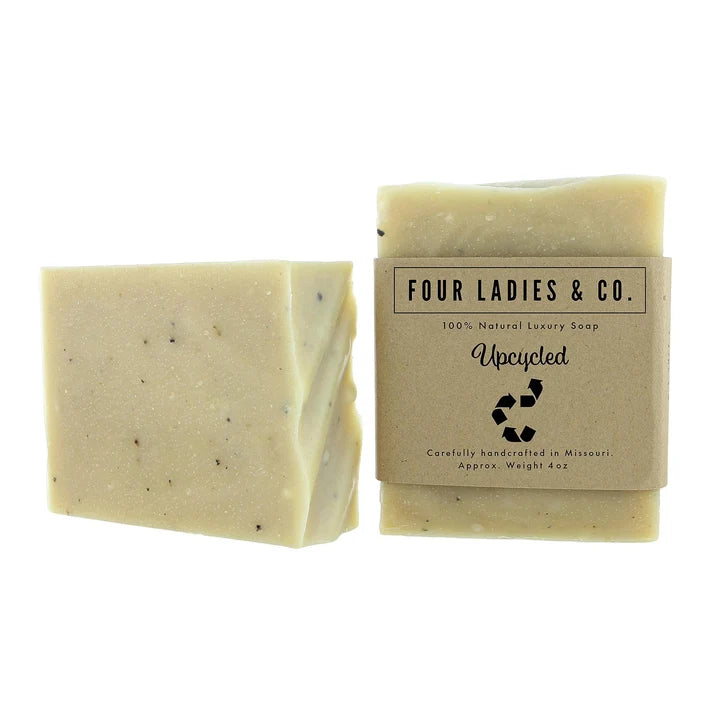 Two bars of Four Ladies & Co. 'Urecycled' natural luxury soap on a white background, one unwrapped showing a speckled cream-colored bar and one wrapped in a kraft paper sleeve.