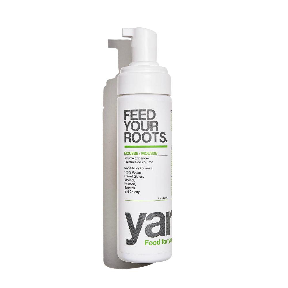 A white pump bottle of yarn Feed Your Roots Mousse on a clean white background, featuring black and green text on the label.