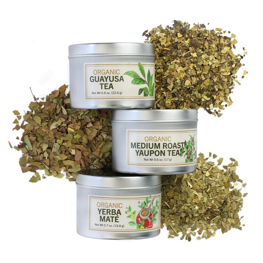 Three metal tea tins labeled 'Guayusa Tea', 'Yaupon Tea', and 'Yerba Mate' with dried tea leaves on a white background.