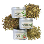Three metal tea tins labeled 'Guayusa Tea', 'Yaupon Tea', and 'Yerba Mate' with dried tea leaves on a white background.