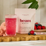 Pink drink in a glass with 'beam Biotic' packaging and berries on a wooden surface.