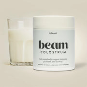 Jar of 'beam Colostrum' supplement next to a glass of milk on a beige background