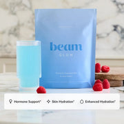 A light blue stand-up pouch labeled 'beam GLOW' stands on a marble surface beside a matching light blue drink in a ribbed glass, with raspberries placed around it. A white banner at the bottom lists benefits: Hormone Support, Skin Hydration, and Enhanced Hydration.