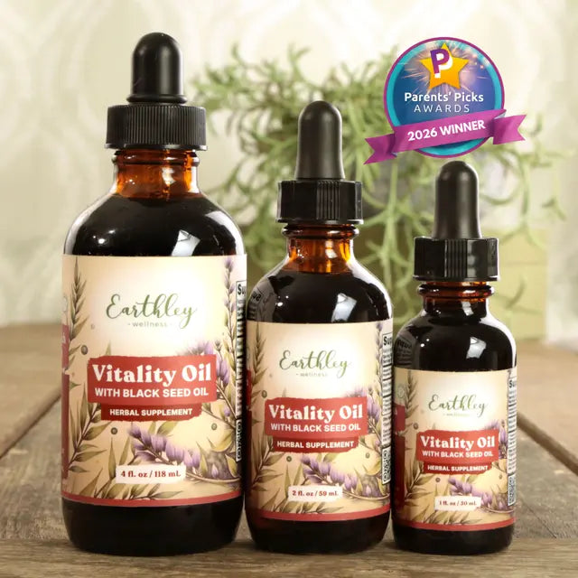 Three bottles of Earthley Vitality Oil with Black Seed Oil on a wooden surface with a blurred green plant background.