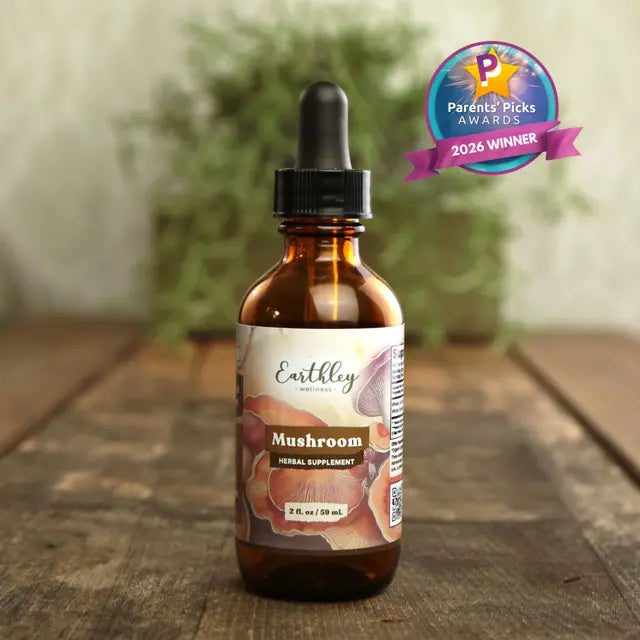 Brown glass bottle with dropper labeled Earthley Mushroom on a wooden surface, with a blurred plant in the background.