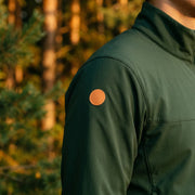 Green jacket with a brown patch on an arm against a blurred forest background