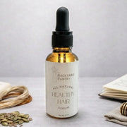 Bottle of 'The Backyard Pantry' healthy hair serum on a light background with natural elements.