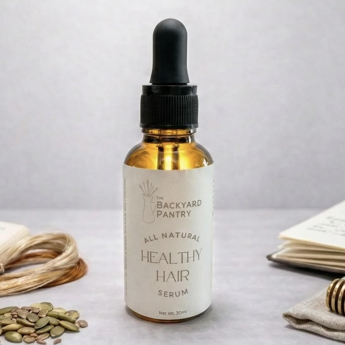 Bottle of 'The Backyard Pantry' healthy hair serum on a light background with natural elements.