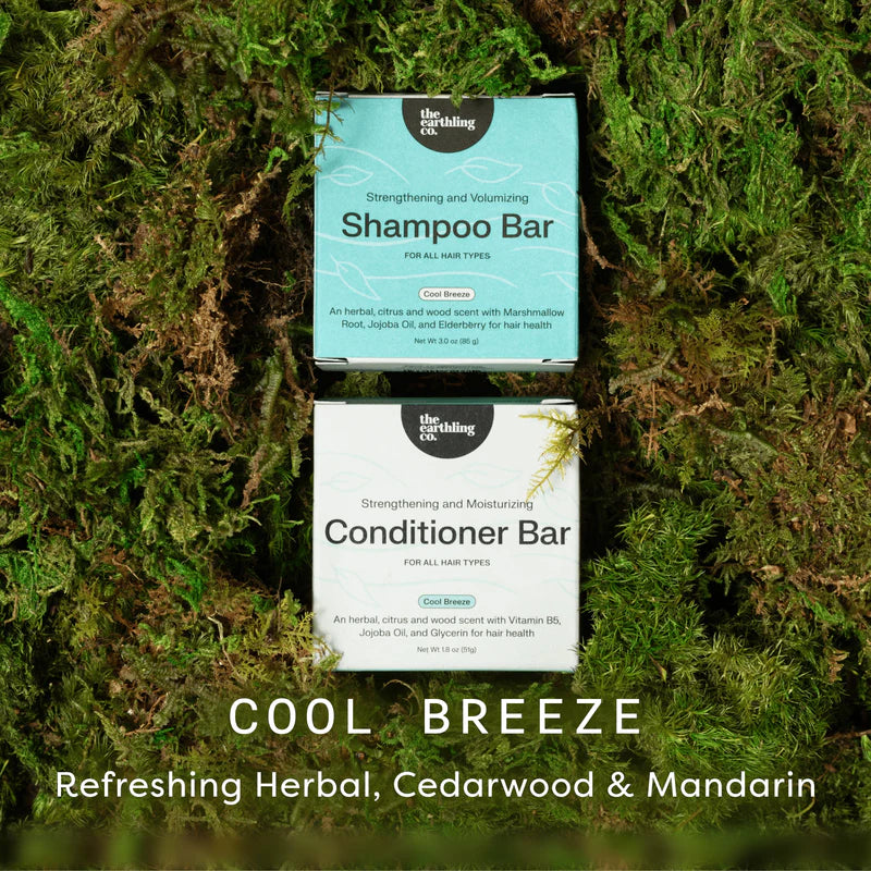 Two packaged hair care bars placed on moss: a light blue Shampoo Bar above and a white Conditioner Bar below. Large text at the bottom reads 'COOL BREEZE' and 'Refreshing Herbal, Cedarwood & Mandarin.
