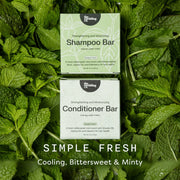 Two boxed hair care bars from The Earthling Co are placed on top of each other among fresh mint leaves. The top box is labeled Shampoo Bar and the bottom box is labeled Conditioner Bar.