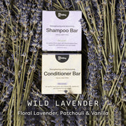Two boxed hair care bars from The Earthling Co, labeled Shampoo Bar and Conditioner Bar, placed on a bed of dried lavender stems. Large text at the bottom reads 'WILD LAVENDER' with 'Floral Lavender, Patchouli & Vanilla' underneath.